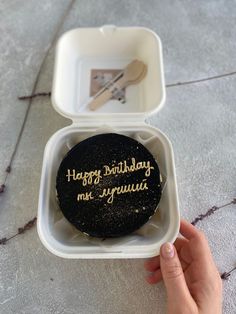 a person holding a black cake in a white container with writing on it and a fork