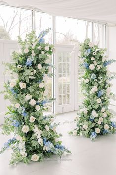 two tall white and blue floral arrangements in front of a large glass window with windowsills