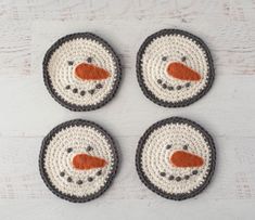 four crocheted snowman coasters sitting on top of a white wooden table