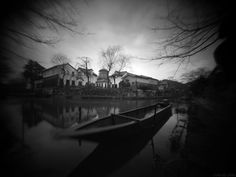 a boat is sitting on the water in front of a house and some trees with no leaves