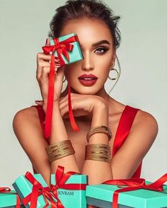 a beautiful woman holding two blue boxes with red ribbons around her neck and wearing gold bracelets