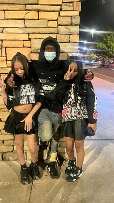 three young women sitting on top of a brick wall wearing face masks and hoods