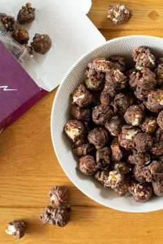 a white bowl filled with chocolate and nuts next to a purple box on top of a wooden table