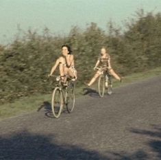 two people riding bikes down a country road