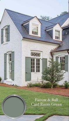 a white house with green shutters on the front and blue roof, surrounded by grass