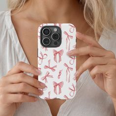 a woman holding up her phone case with pink bows on it, while wearing a white shirt