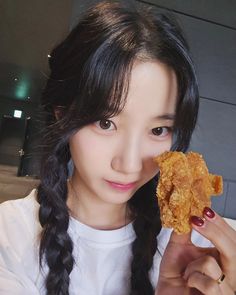 a woman holding up a fried chicken nugget in front of her face and looking at the camera