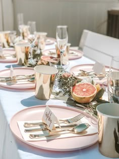 the table is set with plates, silverware and grapefruits on it