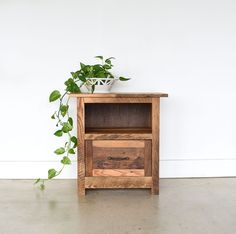 a wooden cabinet with a plant in it on the floor next to a white wall