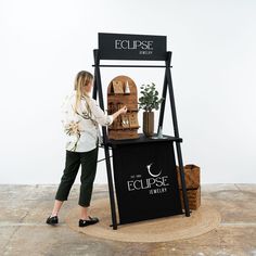 a woman standing next to a table with plants on it and a sign that says eclipse