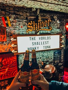 two people holding up beer bottles in front of a sign that says the world's smallest honky tonk