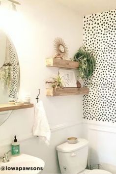 a white toilet sitting next to a sink in a bathroom under a mirror and wooden shelves