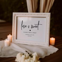 a white framed sign sitting on top of a wooden table next to some burning candles