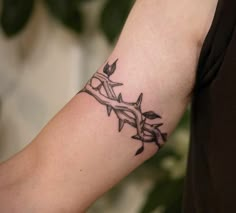 a man with a tattoo on his arm holding onto a barbed wire wristband that has leaves growing out of it