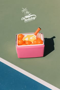 a pink box filled with oranges on top of a tennis court