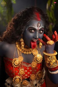 a woman with painted face and gold jewelry on her body, making the peace sign