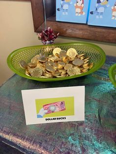 a green bowl filled with gold coins on top of a table next to a sign