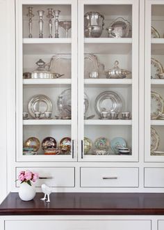 a white china cabinet with glass doors and shelves filled with silverware on top of it