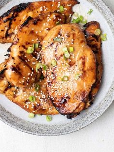 two pieces of chicken with sesame seeds and green onions on a white plate topped with sesame seeds