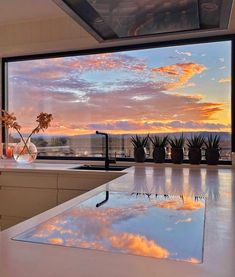 a kitchen with a large window overlooking the ocean and clouds in the sky at sunset