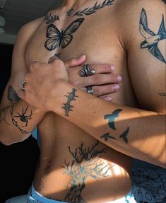 a shirtless man with tattoos on his chest and hands folded in front of him