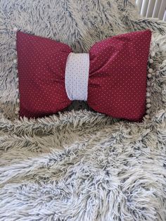 a red pillow with white polka dots and a bow tie on it sitting on a bed