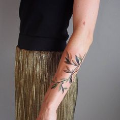 a woman's arm with an olive branch tattoo on her left arm and gold sequin skirt