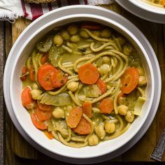 two bowls filled with pasta and vegetables on top of a wooden table next to bread