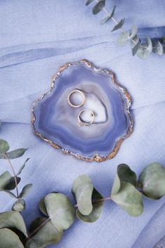 two wedding rings sitting on top of a blue agate shell next to eucalyptus leaves