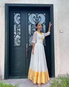 This stunning dress is a true masterpiece of Ethiopian textile art. The lower part of the dress is made from tibeb, a handwoven fabric that is known for its unique patterns and vibrant colors. The intricate design of the tibeb fabric adds a touch of elegance and cultural significance to the dress, making it perfect for special occasions. The neckline of the dress is particularly striking, featuring a cross design that is both traditional and modern at the same time. The cross represents the Ethi Fitted White Cotton Silk Kurta, White Fitted Cotton Silk Kurta, White Cotton Silk Dress With Traditional Drape, White Fitted Cotton Silk Traditional Wear, Handloom Long Sleeve Wedding Dress, Elegant White Cotton Silk Dress, Traditional Floor-length Dresses For Navratri, Ceremonial White Handloom Dress, Semi-stitched Dresses With Zari Work For Traditional Ceremonies