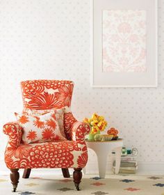 an orange chair sitting in front of a white table with flowers on top of it