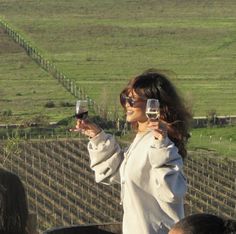 a woman holding up two wine glasses in front of her face while standing next to a barrel