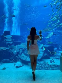 a woman is standing in front of an aquarium looking at the fish swimming around her