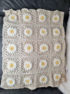 a crocheted blanket with white and yellow daisies on the front, sitting on a black leather couch