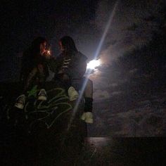 two people sitting on top of a rock at night