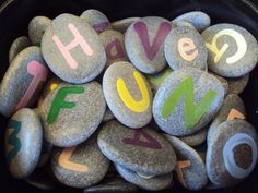 some rocks with the words have fun written on them in different colors and shapes, sitting in a black bowl