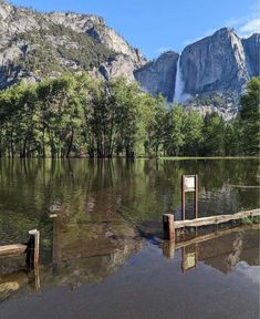 there are two wooden posts in the water and mountains behind them with trees on both sides