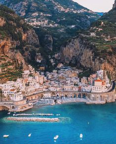 an aerial view of a town on the coast with boats in the water and mountains behind it