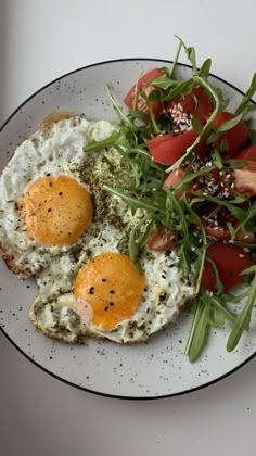 two fried eggs with tomatoes and greens on a plate