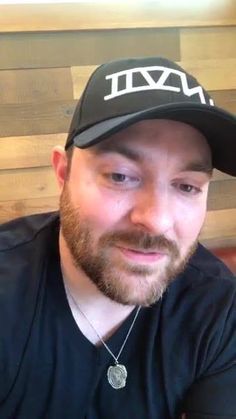 a man with a beard wearing a black hat and looking at the camera while sitting in front of a wooden wall