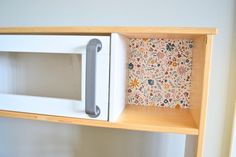 a white microwave oven sitting on top of a wooden shelf next to a flowered wall paper