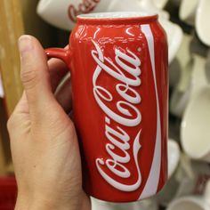 a hand holding a coca - cola can in front of shelves