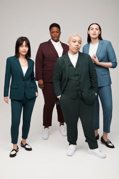 four people standing in front of a white background wearing green suits and black shoes, all looking at the camera