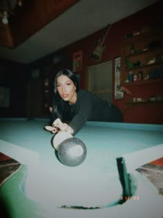 a woman leaning over a pool table with a ball in her hand and one arm extended