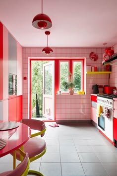 a kitchen with red and pink walls, white tile flooring and an open door leading to the outside