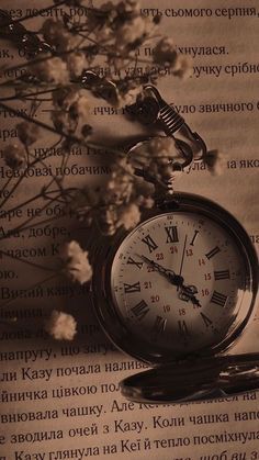 an old pocket watch sitting on top of a piece of paper with flowers in the background