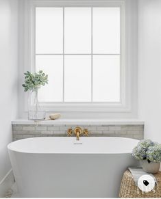 a white bath tub sitting under a window next to a basket with flowers on it