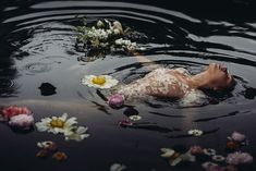 a woman floating on top of a body of water with flowers in the water next to her