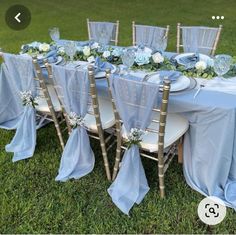 the table is set with blue cloths and flowers on it, along with silver chairs