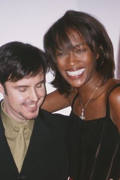 a man standing next to a woman in front of a white wall and smiling at the camera